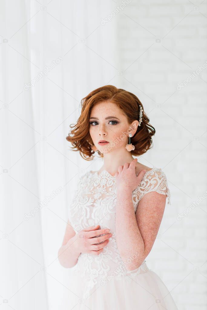 Portrait of red haired girl wearing wedding dress against a white and grey studio background.