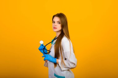 Steteskoplu kadın doktorun portresi sarı arka planda kameraya bakıyor, sağlık hizmetleri