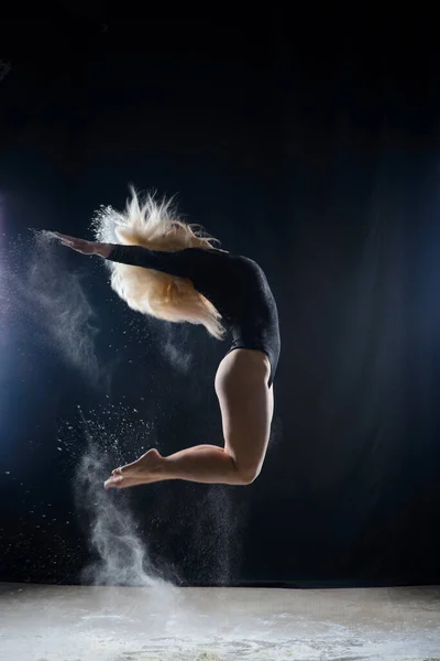 空飛ぶ白い粉の雲で覆われた黒い体操服を着て美しいふっくらブロンドの女の子は 暗闇の上に座って踊るジャンプします 芸術的な概念と広告写真 スペースのコピー — ストック写真