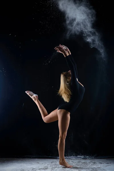 美丽丰满的金发姑娘穿着一身黑色的体操服 身上罩着白粉飘扬的云彩 在黑暗中跳起舞来 艺术性的概念和广告照片 复制空间 — 图库照片
