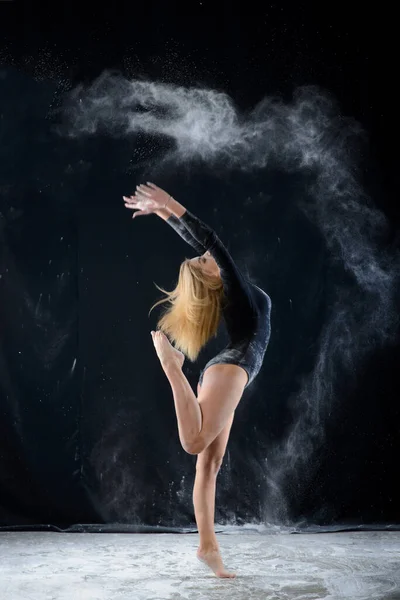 美丽丰满的金发姑娘穿着一身黑色的体操服 身上罩着白粉飘扬的云彩 在黑暗中跳起舞来 艺术性的概念和广告照片 复制空间 — 图库照片