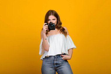 Sarı arka planda kameralı genç bayan fotoğrafçı, gülümsüyor, mutlu..