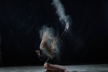 Siyah bir stüdyoda un giymiş, uzun saçlı bir kız..