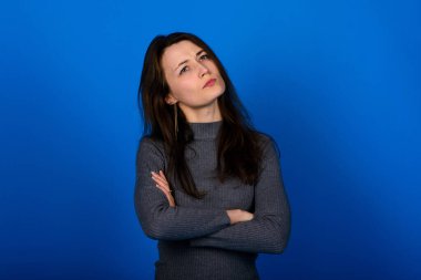 Gülümseyen, mavi arka planda gri elbiseli neşeli genç bir kadının fotoğrafı. Duygusal Portre