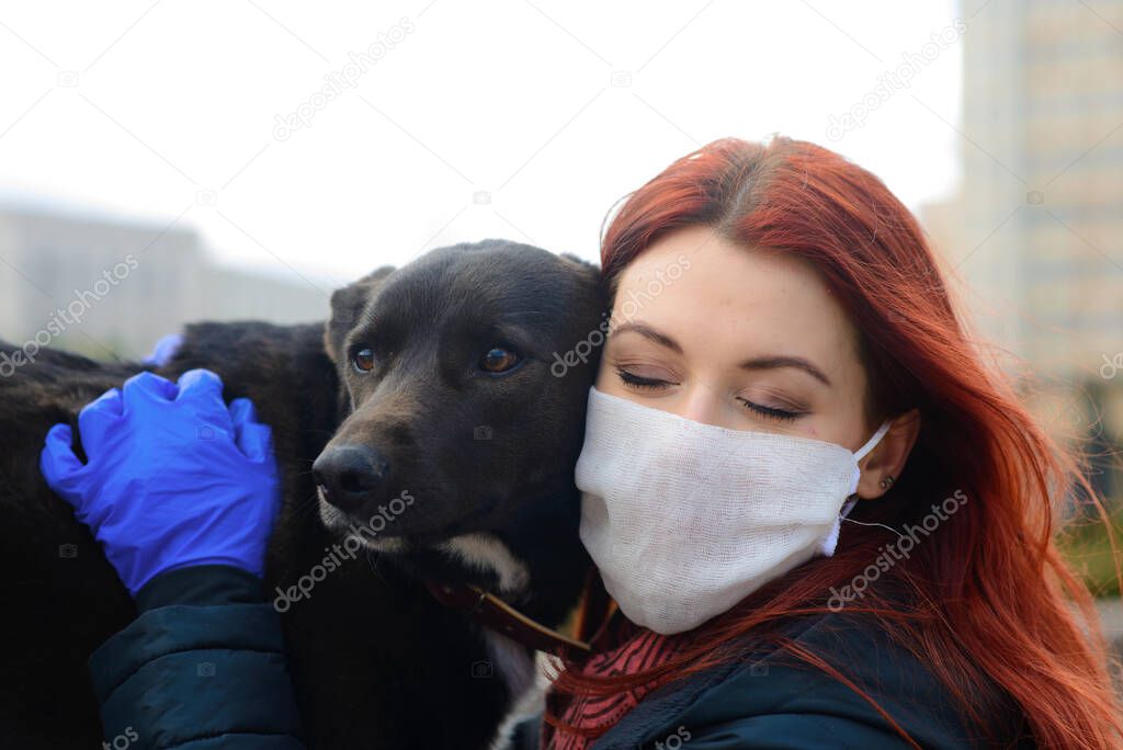 Young female using a face mask as a coronavirus spreading prevention walking with her dog. Global COVID pandemic concept image.