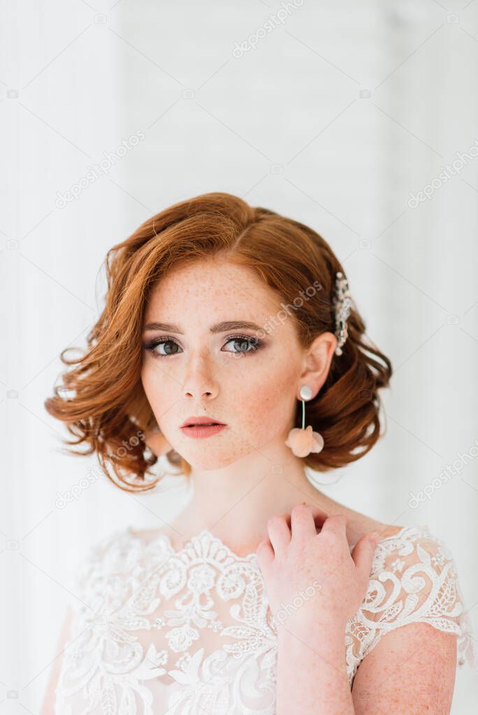 Portrait of red haired girl wearing wedding dress against a white and grey studio background.