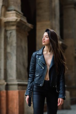 Şık siyah deri ceket giyen güzel esmer bir kadının portresi, şehir arka planında gülümsüyor, mutlu zaman, seyahat konsepti.