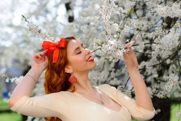 Bahar çiçekleri içinde beyaz elbiseli güzel kızıl saçlı genç kadının portresi.