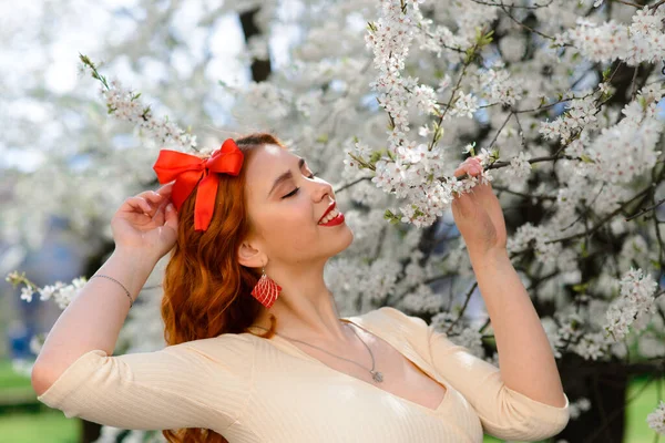 Bahar çiçekleri içinde beyaz elbiseli güzel kızıl saçlı genç kadının portresi.