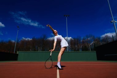 Sahada tenis raketi tutan beyaz elbiseli ve topuklu ayakkabılı seksi kız tenisçi. Genç kadın tenis oynuyor.
