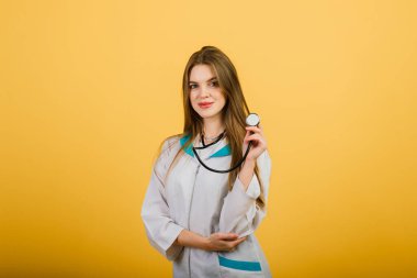 Steteskoplu kadın doktorun portresi sarı arka planda kameraya bakıyor, sağlık hizmetleri