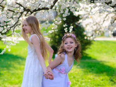 Bahçede beyaz elbiseli, mavi gözlü iki güzel genç kız eğleniyor ve çiçek açan bahar bahçesinin kokusunun tadını çıkarıyorlar..