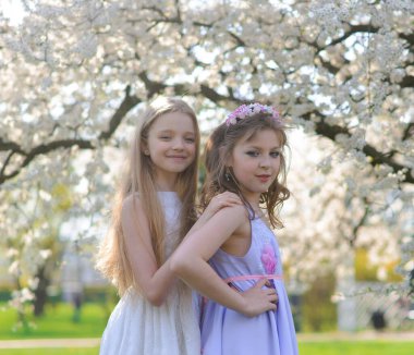 Bahçede beyaz elbiseli, mavi gözlü iki güzel genç kız eğleniyor ve çiçek açan bahar bahçesinin kokusunun tadını çıkarıyorlar..