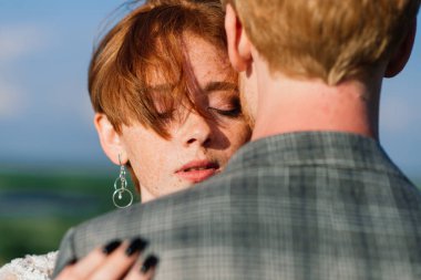 Çok hoş kızıl saçlı genç evli mutlu bir çift gün batımında dışarıda öpüşüyor.