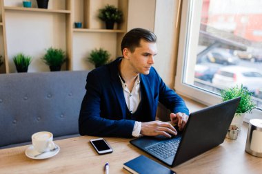 Grip karantinasında yüz maskesi takmış genç yakışıklı iş adamının portresi. Bilgisayarlı, cep telefonlu bir fotoğraf. Koronavirüs salgını.