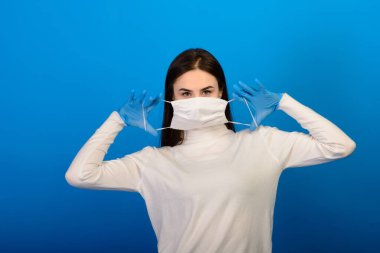Plastik eldiven takan tıbbi maskeli bir kızın portresi. Mavi arkaplan.
