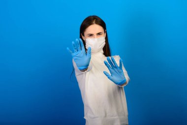 Plastik eldiven takan tıbbi maskeli bir kızın portresi. Mavi arkaplan.