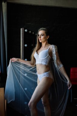 Gelin sabahı hazırlığı. Beyaz gecelikli güzel bir kadın karanlık stüdyoda eğleniyor.