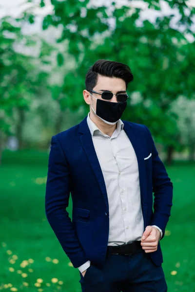 Groom in a medical mask before wedding ceremony in the park outdoors. Weddings during the period of quarantine and pandemic of coronavirus infection