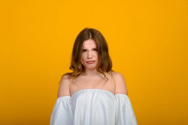 Koyu renk saçlı, gülümseyen ve sarı arka planda poz veren büyük şaşırmış gözleri olan genç bir kadın. Duygusal stüdyo çekimi.