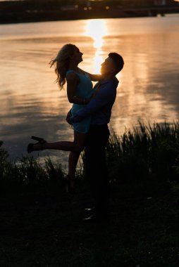 Birbirine aşık çiftler, turuncu gün batımında gölün arkasında hafif bir siluet. Romantik..