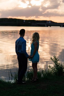 Birbirine aşık çiftler, turuncu gün batımında gölün arkasında hafif bir siluet. Romantik..
