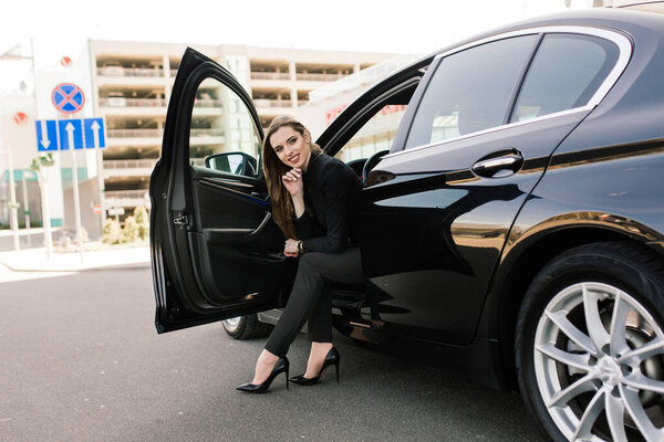 Молодая деловая женщина в черной одежде с дорогой машиной