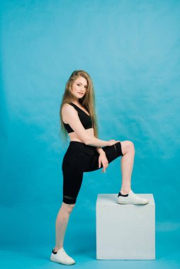 Fitness. Spor kıyafetli bir kadın, bacaklarını açıyor, mavi arka planda ısınıyor..