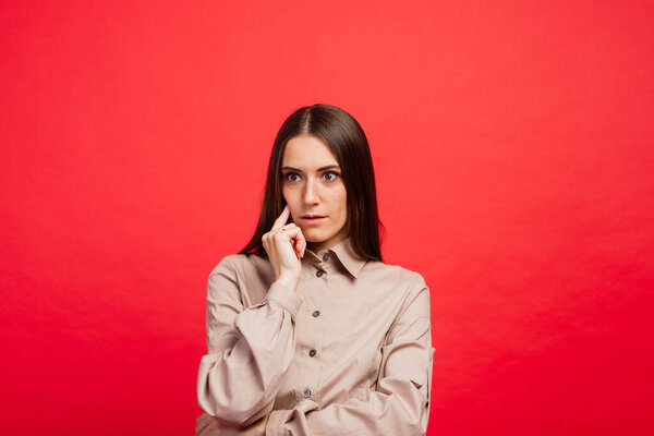 В чем дело? Женский портрет изолирован на красной студии backgroud. Молодая эмоциональная злая, испуганная женщина смотрит в камеру. Человеческие эмоции, концепция выражения лица. Модные цвета