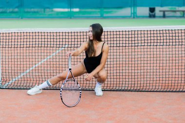 Beautiful young free sports sexy fitness girl dressed in bodysuit, sneakers, with a smart ass and long legs, on a sports ground on a tennis court with a beautiful sky in the background