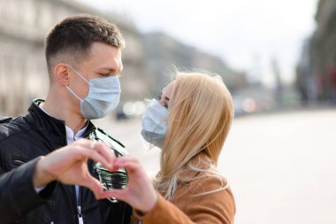 Korumacı tıbbi maske takmış genç bir çift sokakta yüz yüze. Virüs koruması altında bir adam ve kız..