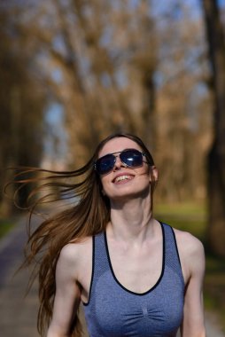 Spor kıyafetleri ve gözlükleriyle parkta güzel bir atletik kız. Sağlıklı bir yaşam tarzı. Yumuşak seçici odak.