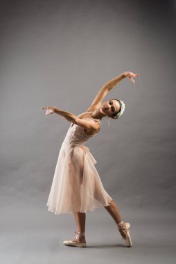 Bej mayo giymiş genç ve güzel bir balerin açık gri stüdyo arka planında poz veriyor.