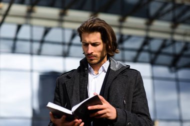 Tam takım elbiseli modern kendine güvenen genç işadamı arka planda şehir manzarasıyla dışarıda duruyor.