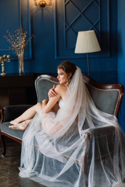 Beyaz dantelli iç çamaşırlı güzel bir gelin, bir otel odasında çıplak omuzlu, yatak odasında oturuyor. Mutlu düğün sabahları..