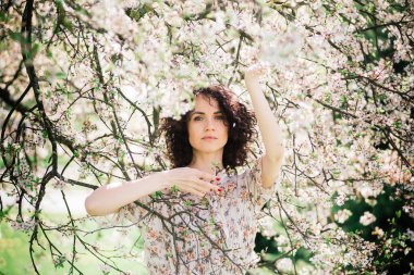 Bahar çiçekli bahçede poz veren kıvırcık saçlı çekici bir kadın.