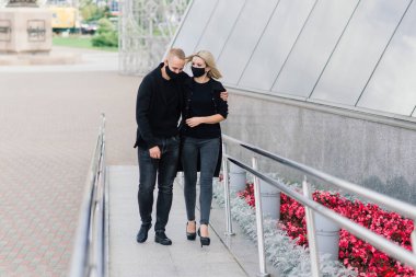 Coronavirus salgını karantinası sırasında Avrupa şehrinin boş sokaklarında gezen modaya uygun koruyucu maskeler, kot ceketler giyen çift.