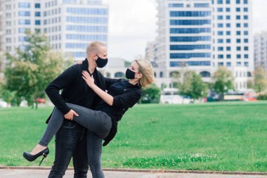 Coronavirus salgını karantinası sırasında Avrupa şehrinin boş sokaklarında gezen modaya uygun koruyucu maskeler, kot ceketler giyen çift.