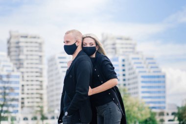 Coronavirus salgını karantinası sırasında Avrupa şehrinin boş sokaklarında gezen modaya uygun koruyucu maskeler, kot ceketler giyen çift.