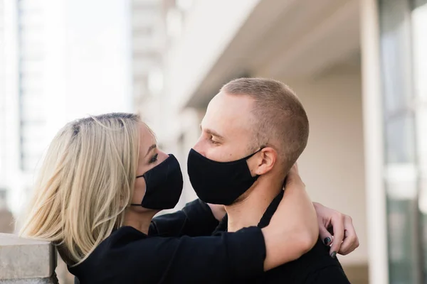 Couple wearing trendy fashionable protective masks, denim jackets, walking in empty street of European city during quarantine of coronavirus outbreak.