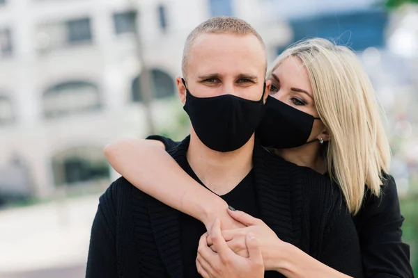 Couple wearing trendy fashionable protective masks, denim jackets, walking in empty street of European city during quarantine of coronavirus outbreak.