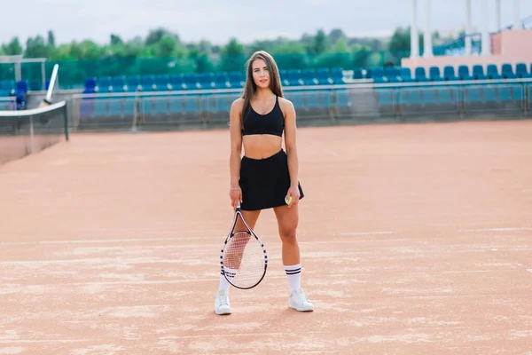网球场上的美女穿着黑色时髦运动服 手持网球拍站在室外场地上的时尚性感女孩的画像 — 图库照片