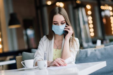 Takım elbiseli ve tıbbi maskeli kadın yönetici sokak kafesinde çalışıyor..
