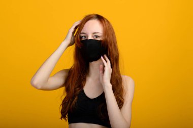 Plastik eldiven takan tıbbi maskeli bir kızın portresi. Sarı ve gri arkaplan.
