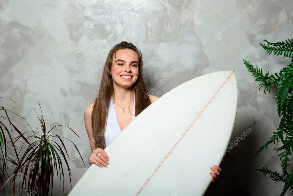 Beautiful young woman posing with surfboard in studio