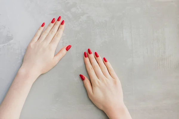 Isolated woman\'s hands with red nails in front of a grey wall