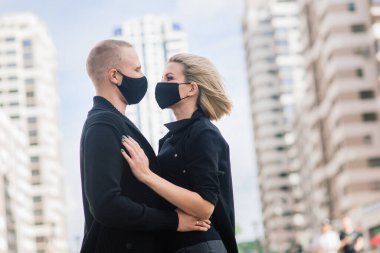 Karantina sırasında şehrin boş sokaklarında yürüyen şık koruyucu maskeler takan bir çift..