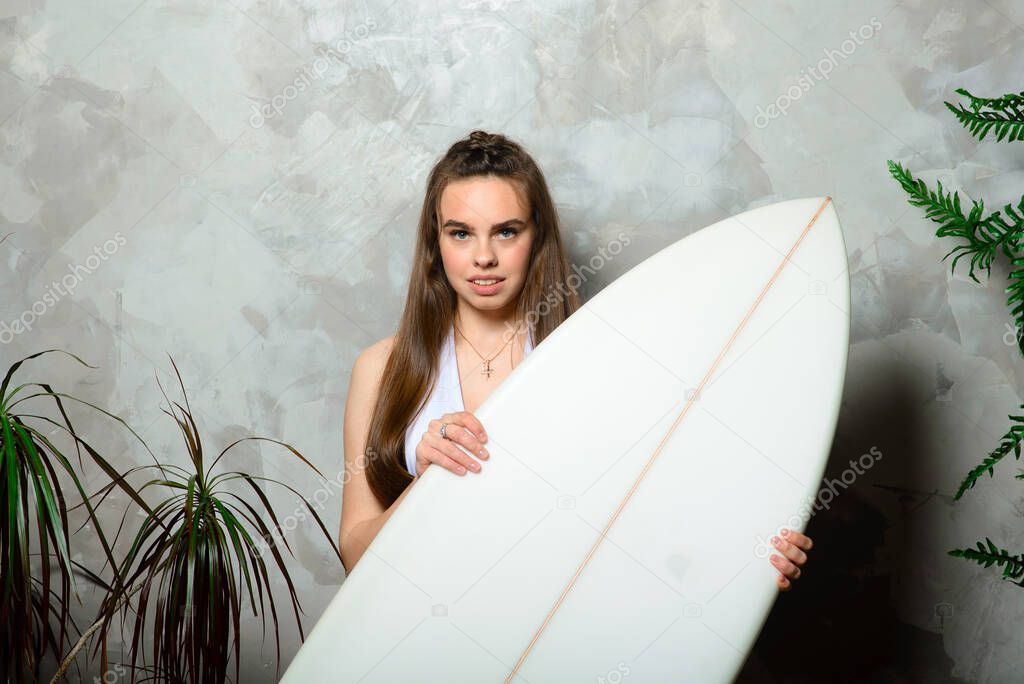 Beautiful young woman posing with surfboard in studio