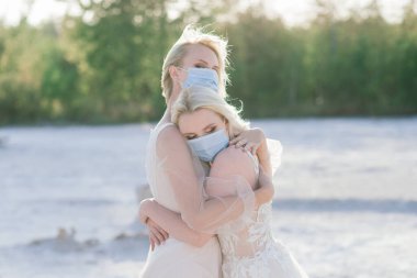 Lezbiyen çift beyaz kumda evleniyor, salgın COVID-19 'u önlemek için maske takıyorlar.