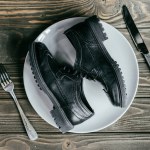 Shoes lying on plate with cutlery on wooden table